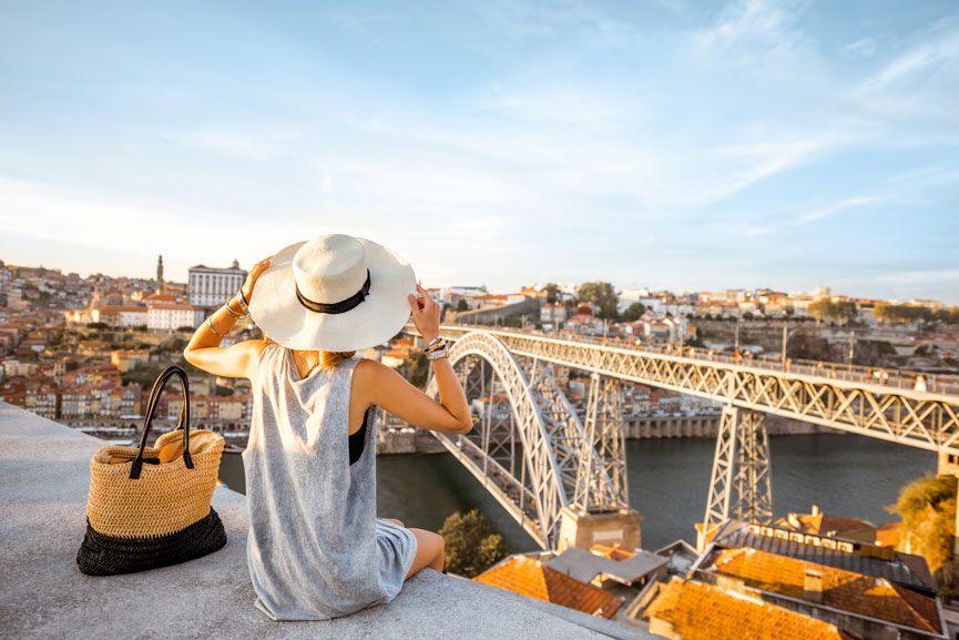 senhora turista de chapéu sentada em miradouro com vista para a Ponte S. Luís no Porto Portugal turismo exportação de serviços aumentou 