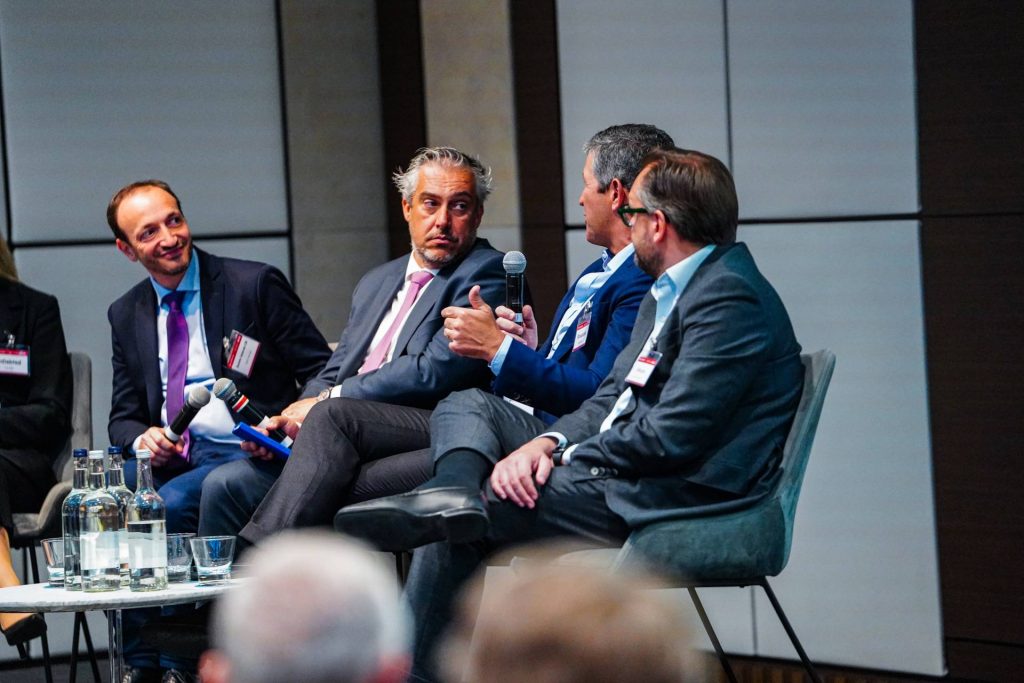 Event NPL Europe in London by SmithNovak Hugo Velez Managing Director from Hipoges Speaks Man holding microphone on stage conference debate REO market Servicing panel discussion