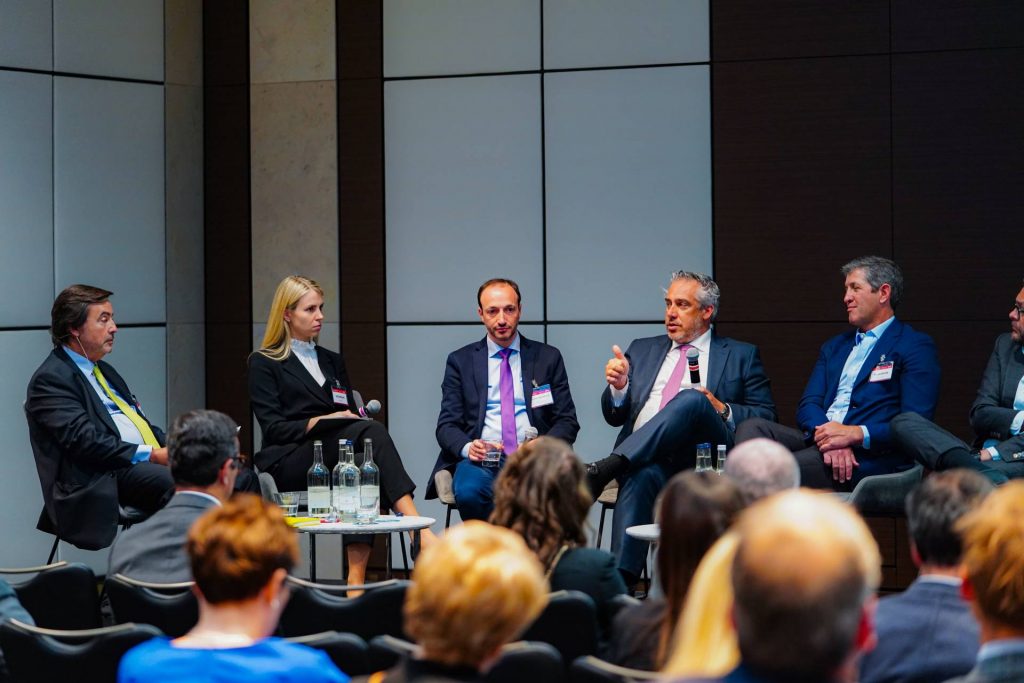 Event NPL Europe in London by SmithNovak Hugo Velez Managing Director from Hipoges speaker at conference debate REO market Servicing panel discussion Man holding microphone on stage speaking to group of eclectic people