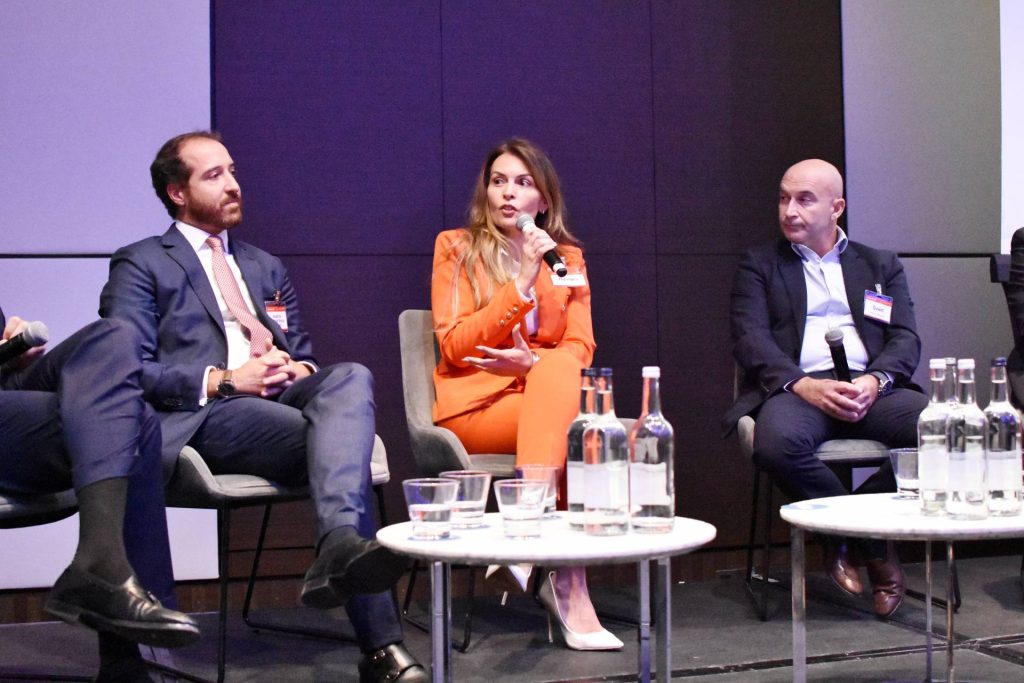 event Global NPL in London by SmithNovak Margarida Maia CSO of Hipoges at the panel on the Servicing REO's NPLs markets conversation woman holding microphone on stage speaking to eclectic group of people man